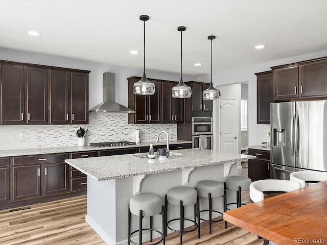 kitchen featuring light wood-style floors, wall chimney range hood, backsplash, and stainless steel appliances