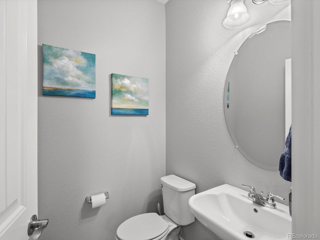bathroom with toilet, a textured wall, and a sink