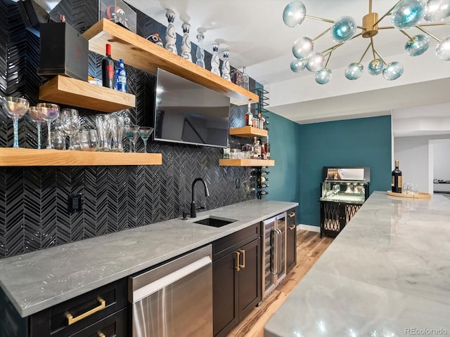 bar featuring stainless steel dishwasher, tasteful backsplash, wet bar, a sink, and light wood finished floors