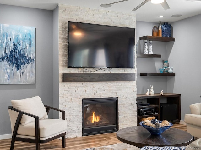 living room with wood finished floors, baseboards, a ceiling fan, and a stone fireplace