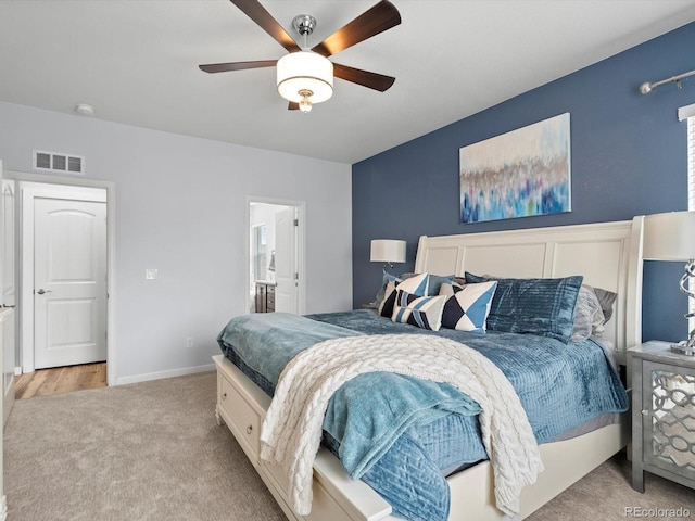 bedroom with ensuite bathroom, light colored carpet, a ceiling fan, visible vents, and baseboards
