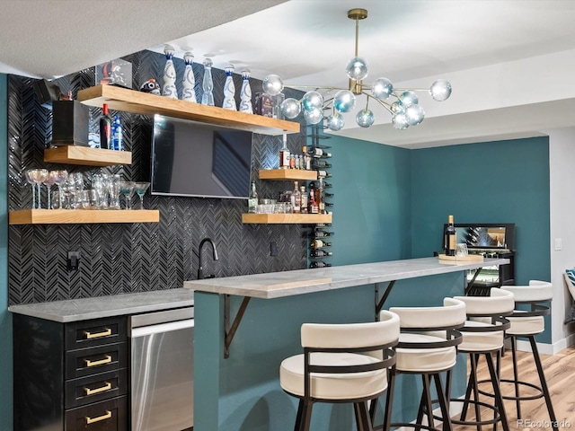 bar featuring light wood-style floors, stainless steel dishwasher, indoor wet bar, a chandelier, and backsplash