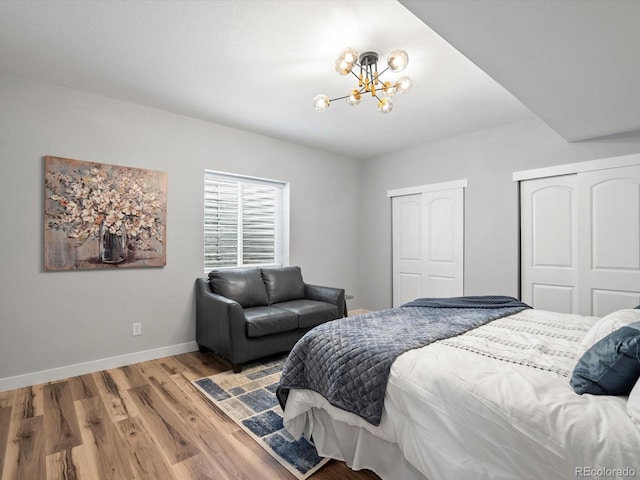 bedroom featuring two closets, baseboards, an inviting chandelier, and wood finished floors