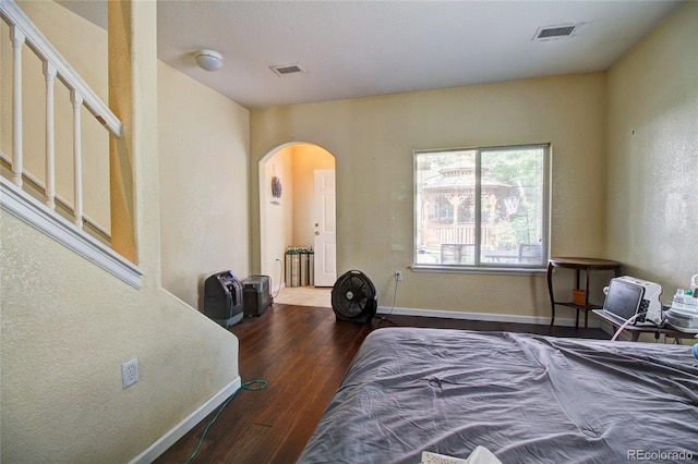 bedroom with arched walkways, visible vents, baseboards, and wood finished floors