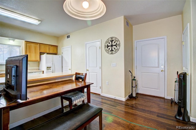 kitchen with dark wood-style flooring, baseboards, visible vents, and white fridge with ice dispenser