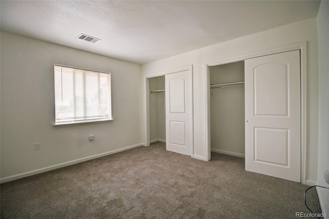 unfurnished bedroom featuring carpet, baseboards, visible vents, multiple closets, and a textured ceiling