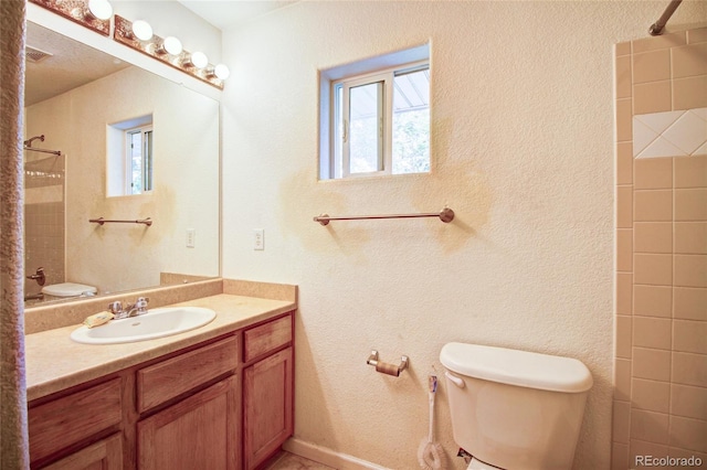 full bathroom with a tile shower, toilet, vanity, and a textured wall