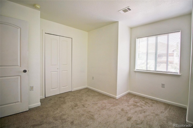 unfurnished bedroom featuring carpet flooring, baseboards, visible vents, and a closet