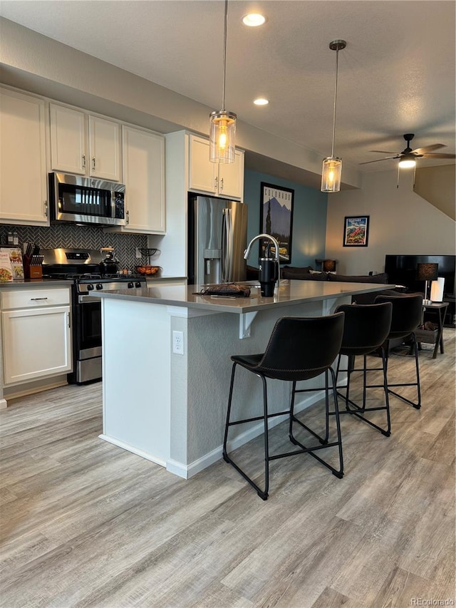 kitchen with pendant lighting, white cabinets, stainless steel appliances, and an island with sink