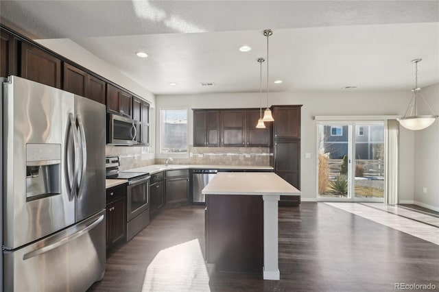 kitchen featuring dark brown cabinetry, dark wood-style floors, a center island, stainless steel appliances, and backsplash