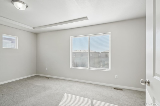 carpeted empty room with a tray ceiling, visible vents, and baseboards