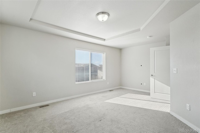 carpeted empty room featuring a raised ceiling, visible vents, and baseboards