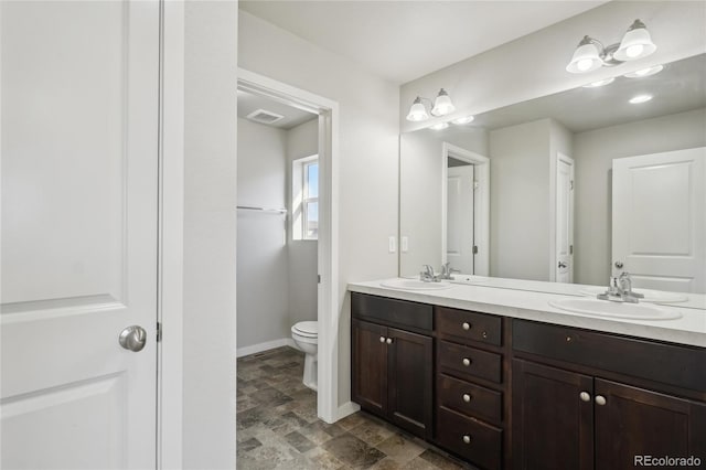 bathroom featuring toilet, a sink, visible vents, baseboards, and double vanity