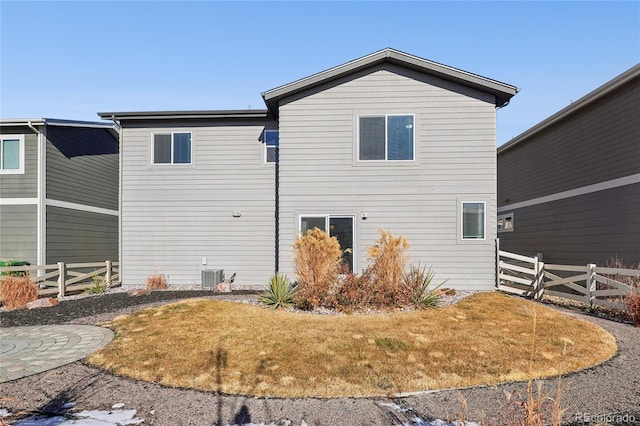 rear view of property with central AC unit, a lawn, and fence