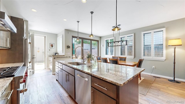 1426 S Pearl St, Denver, CO 80210 - kitchen with appliances with stainless steel finishes, light wood-style flooring, wall chimney range hood, a kitchen island with sink, and decorative light fixtures