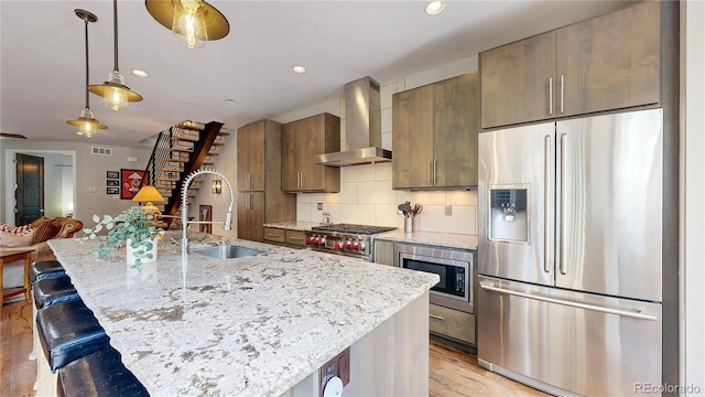 1426 S Pearl St, Denver, CO 80210 - kitchen with appliances with stainless steel finishes, wall chimney exhaust hood, light wood-style floors, a kitchen bar, and recessed lighting