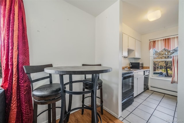 kitchen with white cabinets, baseboard heating, black appliances, and light tile patterned floors