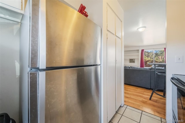 kitchen featuring white cabinets, light tile patterned floors, stainless steel refrigerator, and black electric range