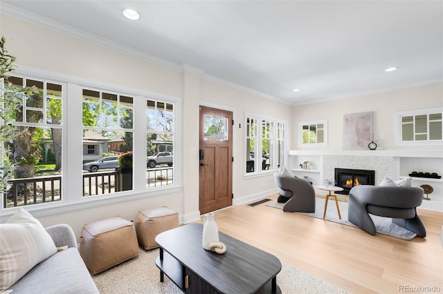 living area with wood finished floors, a glass covered fireplace, ornamental molding, recessed lighting, and baseboards