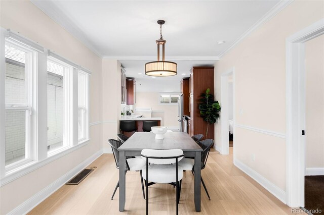 dining area featuring light wood-style floors, baseboards, and ornamental molding