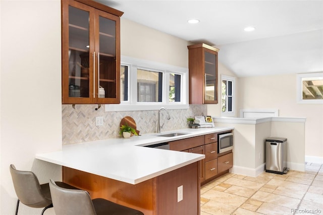 kitchen featuring a sink, stainless steel microwave, a peninsula, backsplash, and vaulted ceiling