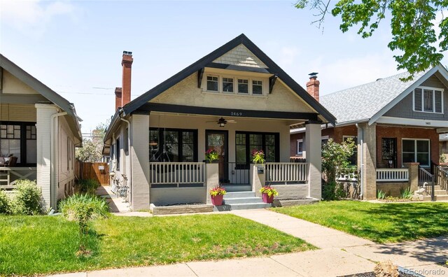 view of front of home featuring a porch, a front lawn, ceiling fan, and a chimney