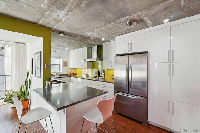 kitchen featuring a kitchen breakfast bar, stainless steel appliances, dark hardwood / wood-style floors, wall chimney exhaust hood, and white cabinets