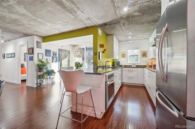 kitchen with white cabinets, kitchen peninsula, dark hardwood / wood-style flooring, a breakfast bar, and appliances with stainless steel finishes