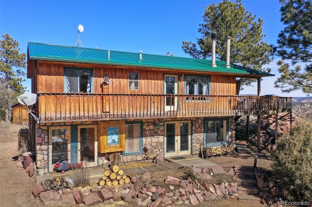 view of front of home featuring a wooden deck, stone siding, french doors, and metal roof