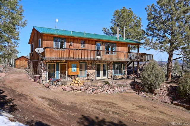 rear view of house featuring a wooden deck, stone siding, and metal roof