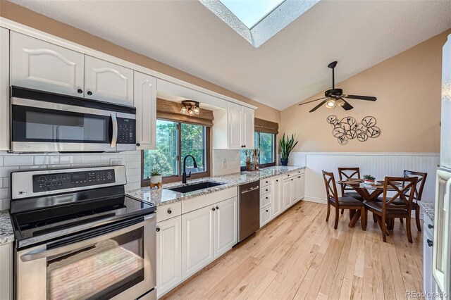 3752 S Helena Way, Aurora, CO 80013 - kitchen with appliances with stainless steel finishes, white cabinetry, wainscoting, light wood finished floors, and a skylight