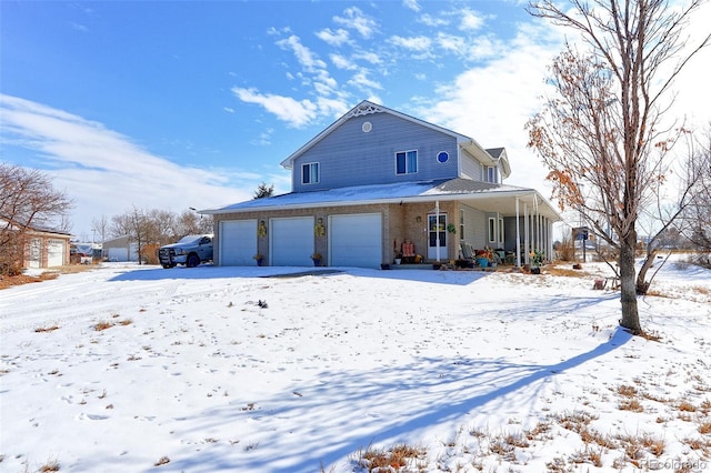 snow covered rear of property featuring a porch and a garage