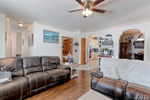 living area featuring light wood-type flooring, arched walkways, a textured ceiling, and a ceiling fan