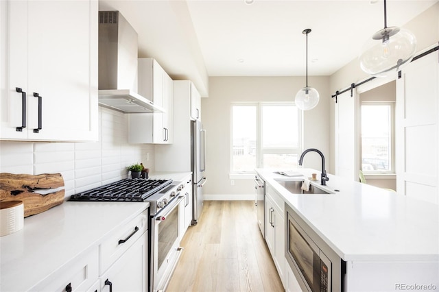 kitchen with a center island with sink, a sink, backsplash, appliances with stainless steel finishes, and wall chimney range hood