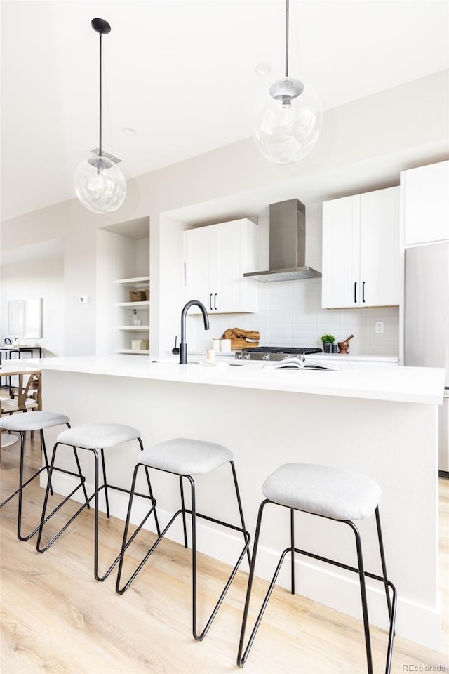 kitchen with wall chimney range hood, light wood-type flooring, white cabinets, stainless steel fridge, and a sink