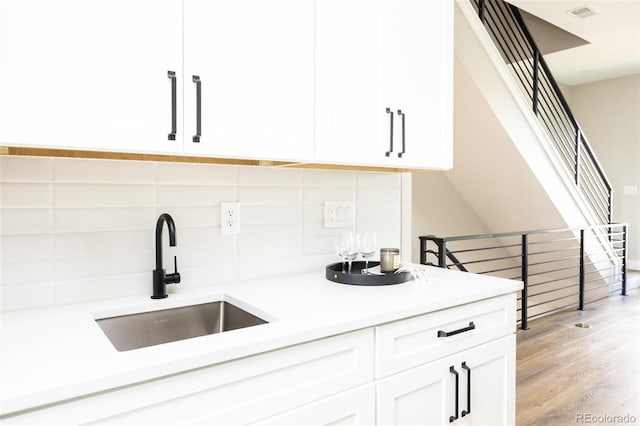 kitchen featuring visible vents, light wood finished floors, a sink, decorative backsplash, and white cabinetry