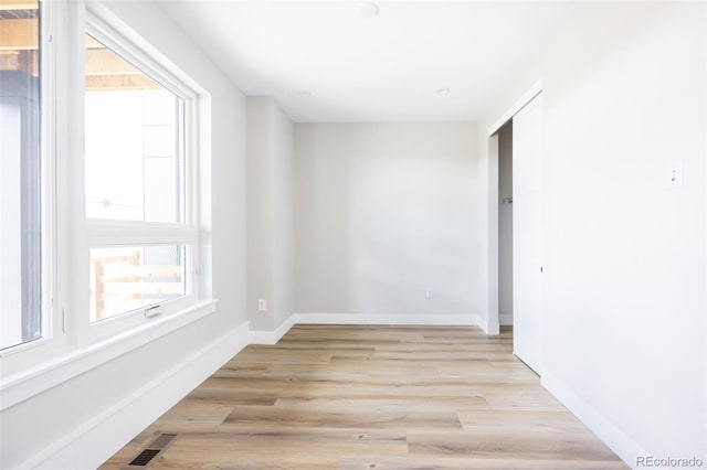 unfurnished room featuring plenty of natural light, baseboards, light wood-type flooring, and visible vents