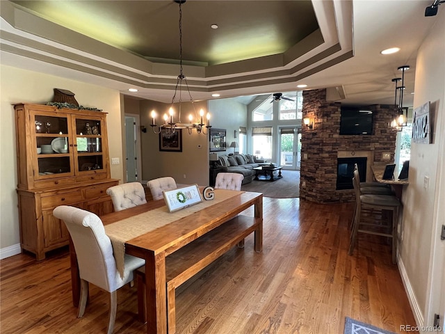 dining space featuring a fireplace, hardwood / wood-style flooring, ceiling fan with notable chandelier, and a raised ceiling