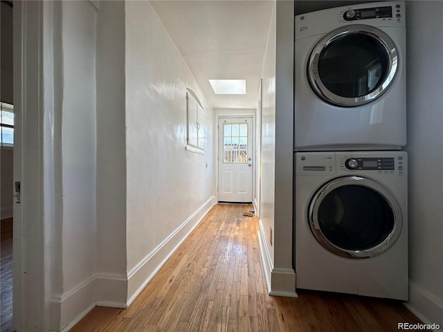 clothes washing area with a skylight, hardwood / wood-style flooring, and stacked washer and dryer