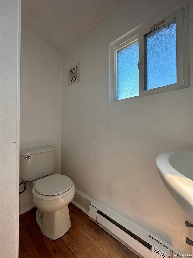 bathroom featuring wood-type flooring, toilet, and a baseboard heating unit