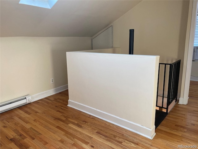 interior space with a baseboard radiator, lofted ceiling with skylight, and light wood-type flooring