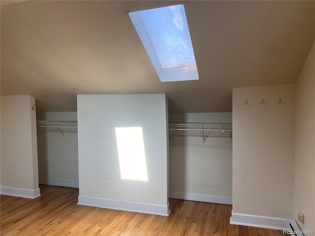 unfurnished bedroom with light wood-type flooring, lofted ceiling with skylight, and a baseboard heating unit