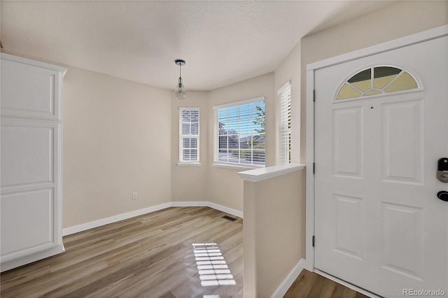 foyer entrance featuring baseboards, visible vents, wood finished floors, and a textured ceiling