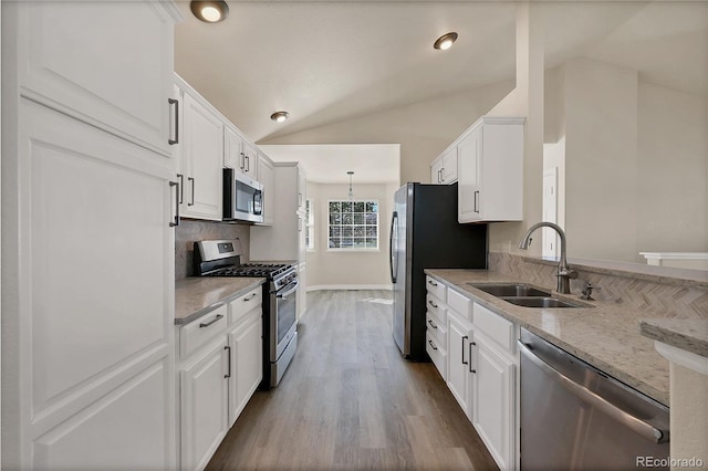 kitchen featuring appliances with stainless steel finishes, light stone counters, white cabinets, lofted ceiling, and sink