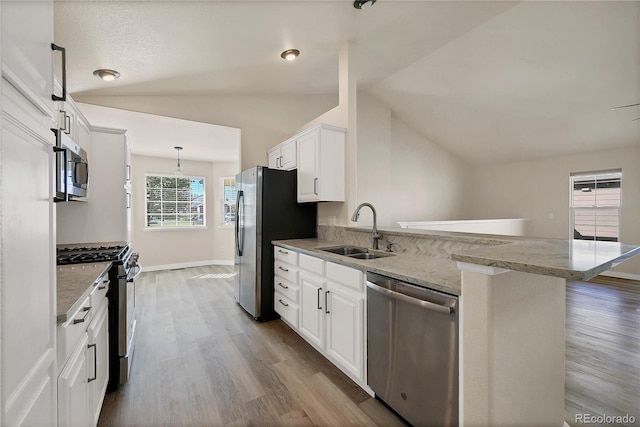 kitchen with white cabinetry, lofted ceiling, stainless steel appliances, a sink, and a peninsula