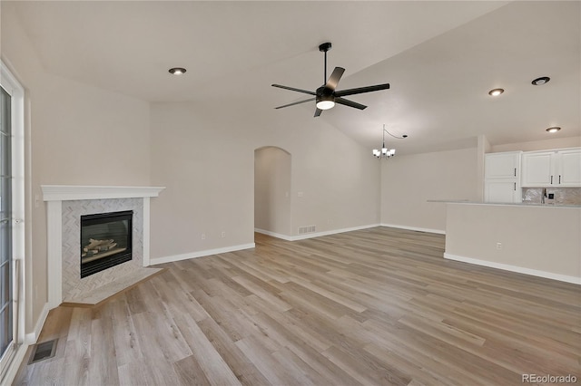 unfurnished living room with ceiling fan with notable chandelier, a fireplace, vaulted ceiling, and light hardwood / wood-style flooring