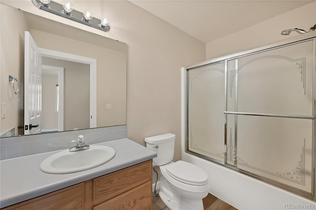 full bathroom with hardwood / wood-style floors, combined bath / shower with glass door, vanity, and toilet