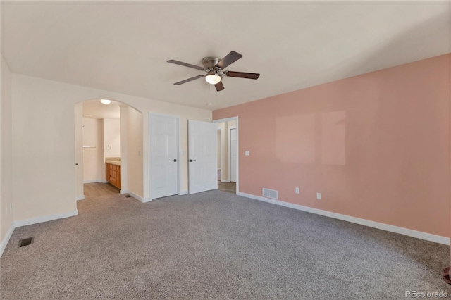carpeted empty room with arched walkways, baseboards, ceiling fan, and visible vents