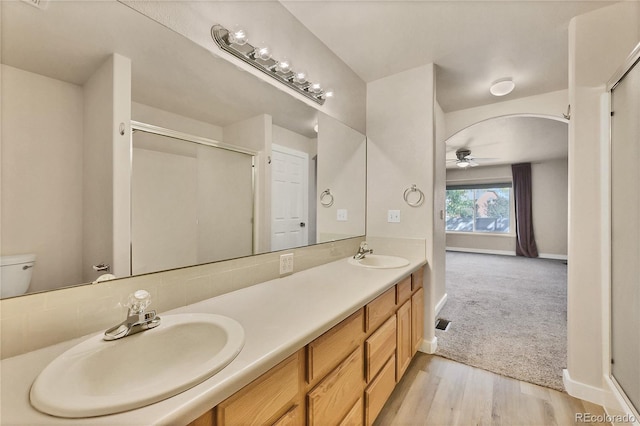 bathroom featuring vanity, wood-type flooring, ceiling fan, a shower with door, and toilet