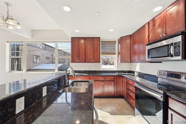 kitchen featuring sink, dark stone counters, decorative light fixtures, light tile patterned floors, and appliances with stainless steel finishes